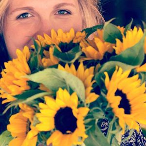 A lady holding a bunch of sunflowers near her face