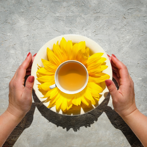 Hands holding a teacup with a sunflower on the saucer